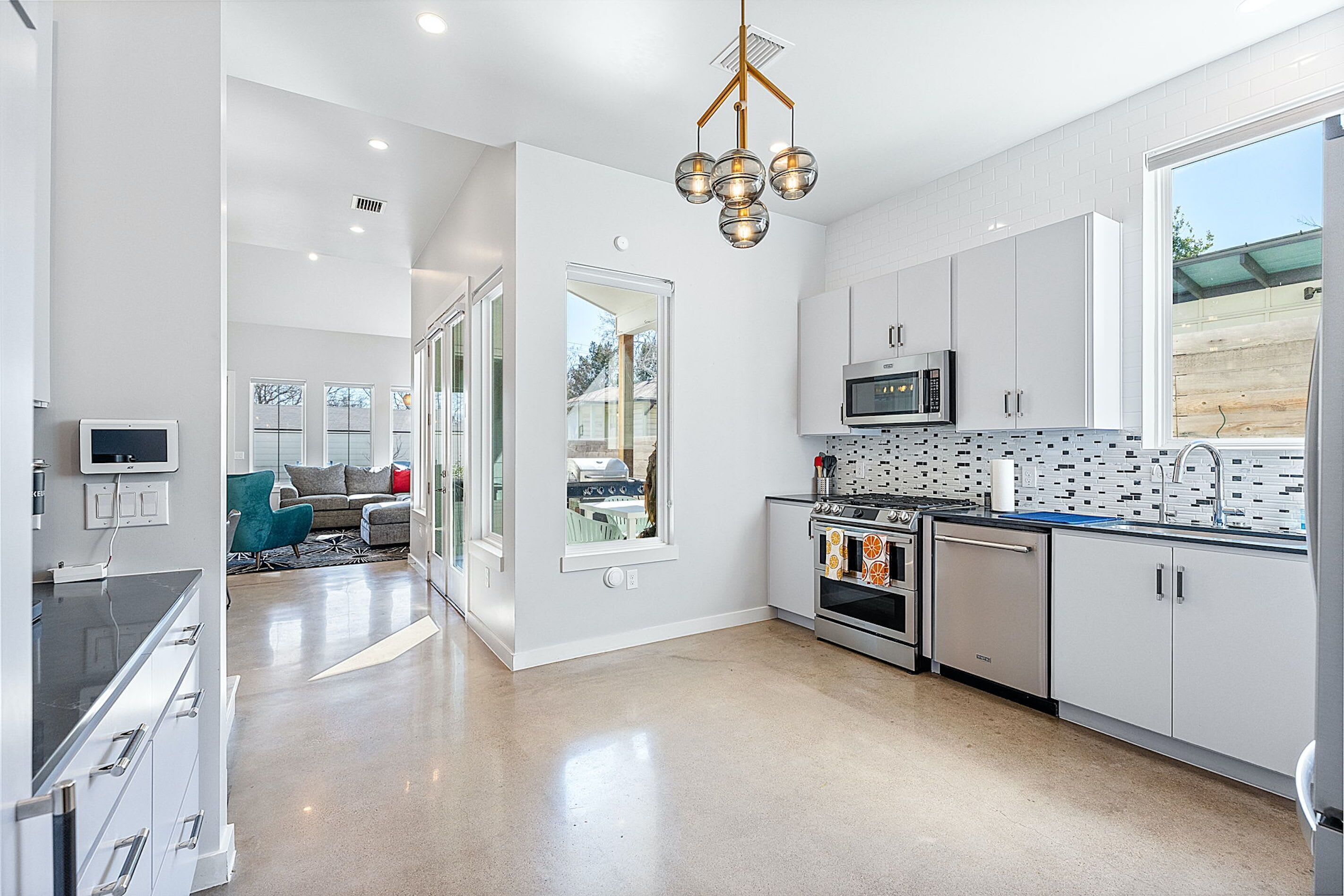 A modern kitchen with white cabinets, stainless steel appliances, and a unique pendant light.