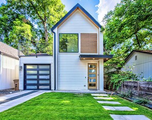 A modern two-story house with a garage, a front door with glass panels, and a well-maintained lawn with stepping stones. - Private Backyard | Short & Long Stays in East ATX (Austin)
