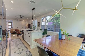 Une cuisine moderne dotée d’un îlot central, d’un coin repas avec une table en bois et d’une vue sur le jardin arrière.