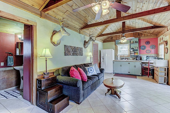 A rustic interior with a wooden ceiling, a sofa, a dining table, and a kitchen area.