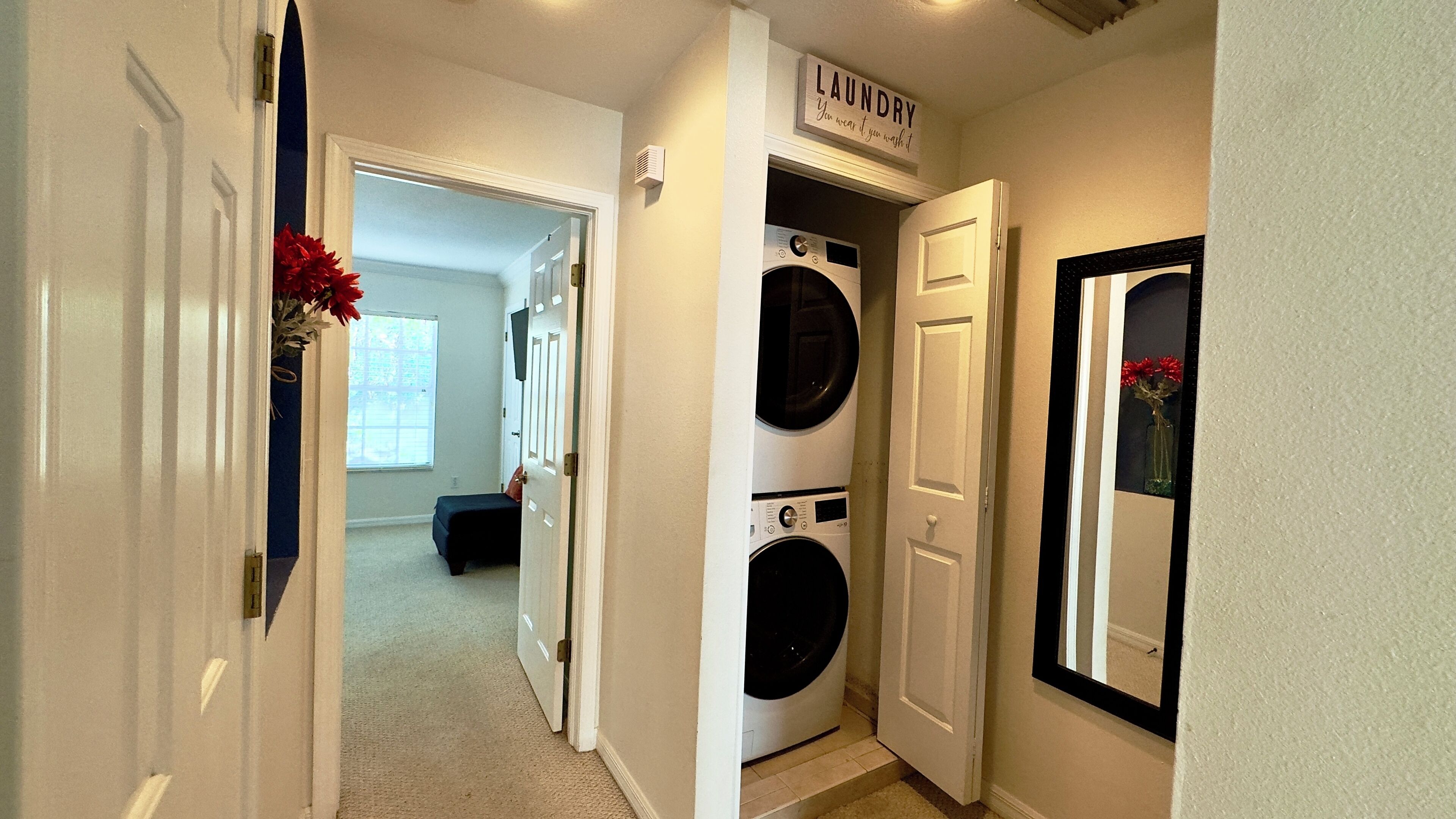 A laundry room with two stacked front-loading washers and dryers, a sign above the dryers that reads "LAUNDRY," and a door leading to another room.