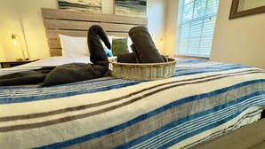 A bed with a striped blanket, a wicker basket with towels, and a wooden headboard.