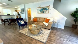 A living room with a sofa, armchair, coffee table, and a dining area with chairs and a table.