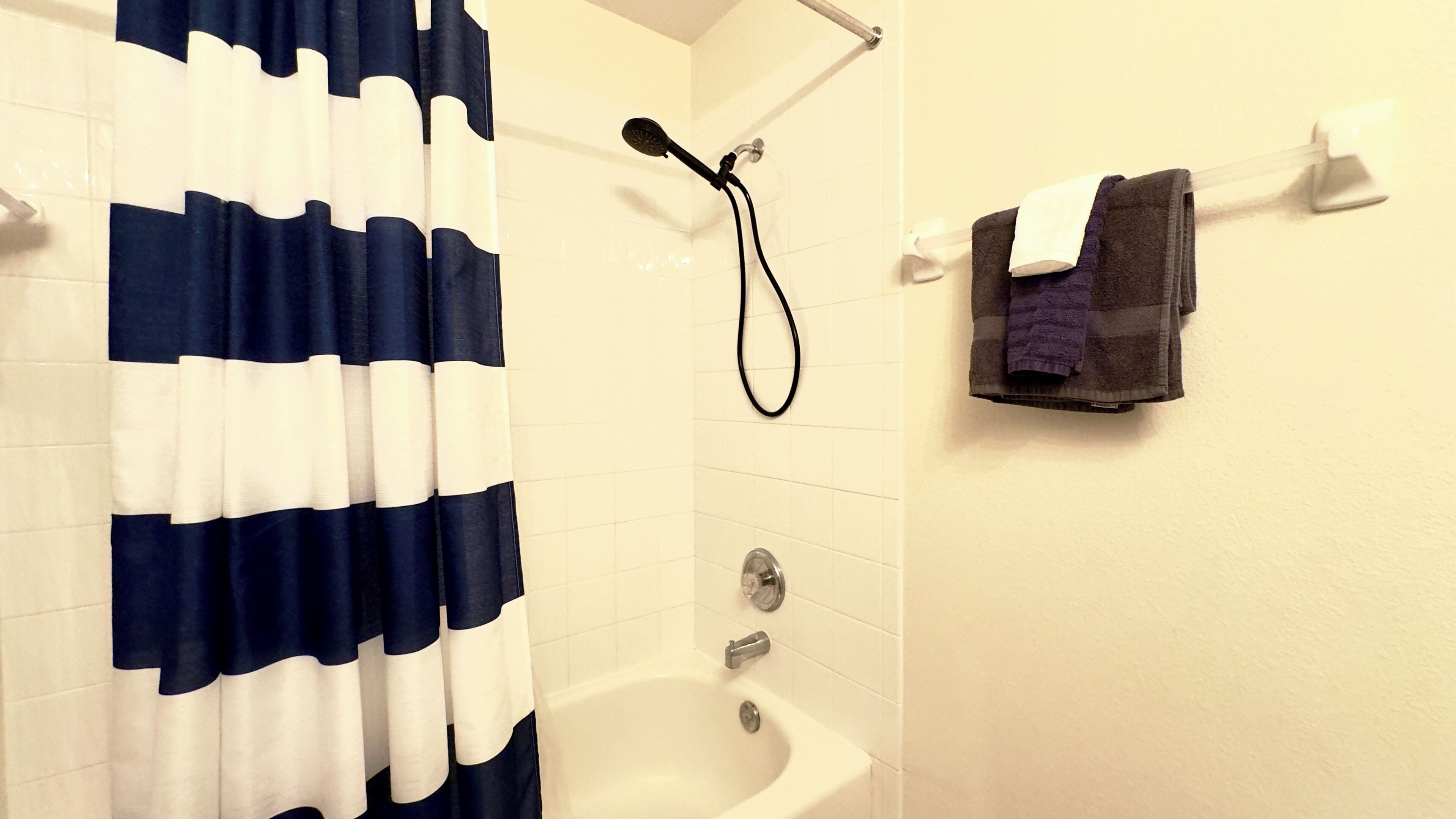 A bathroom with a white and blue striped shower curtain, a white bathtub, and a towel rack with a dark towel.