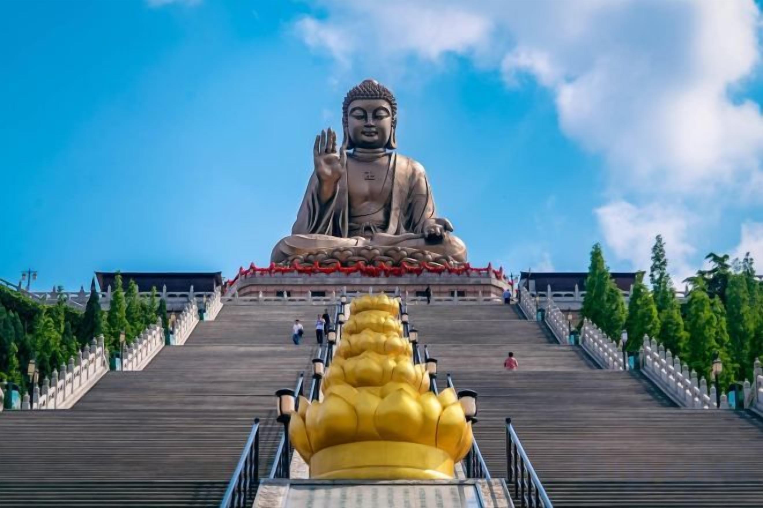 A large Buddha statue at the top of a staircase with a golden statue in the foreground.