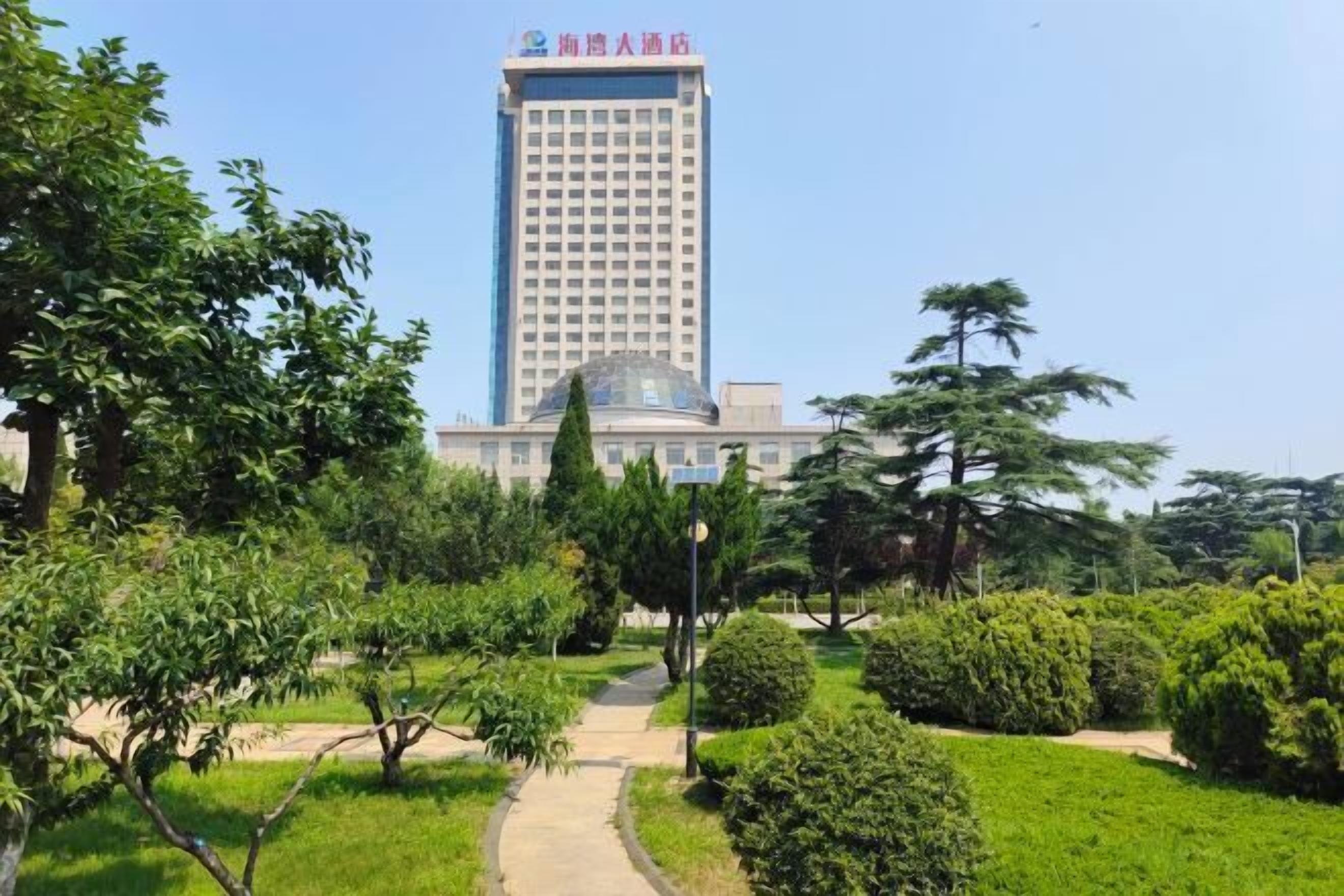 Un hotel con un edificio alto, rodeado de un jardín bien cuidado con varios árboles y arbustos.