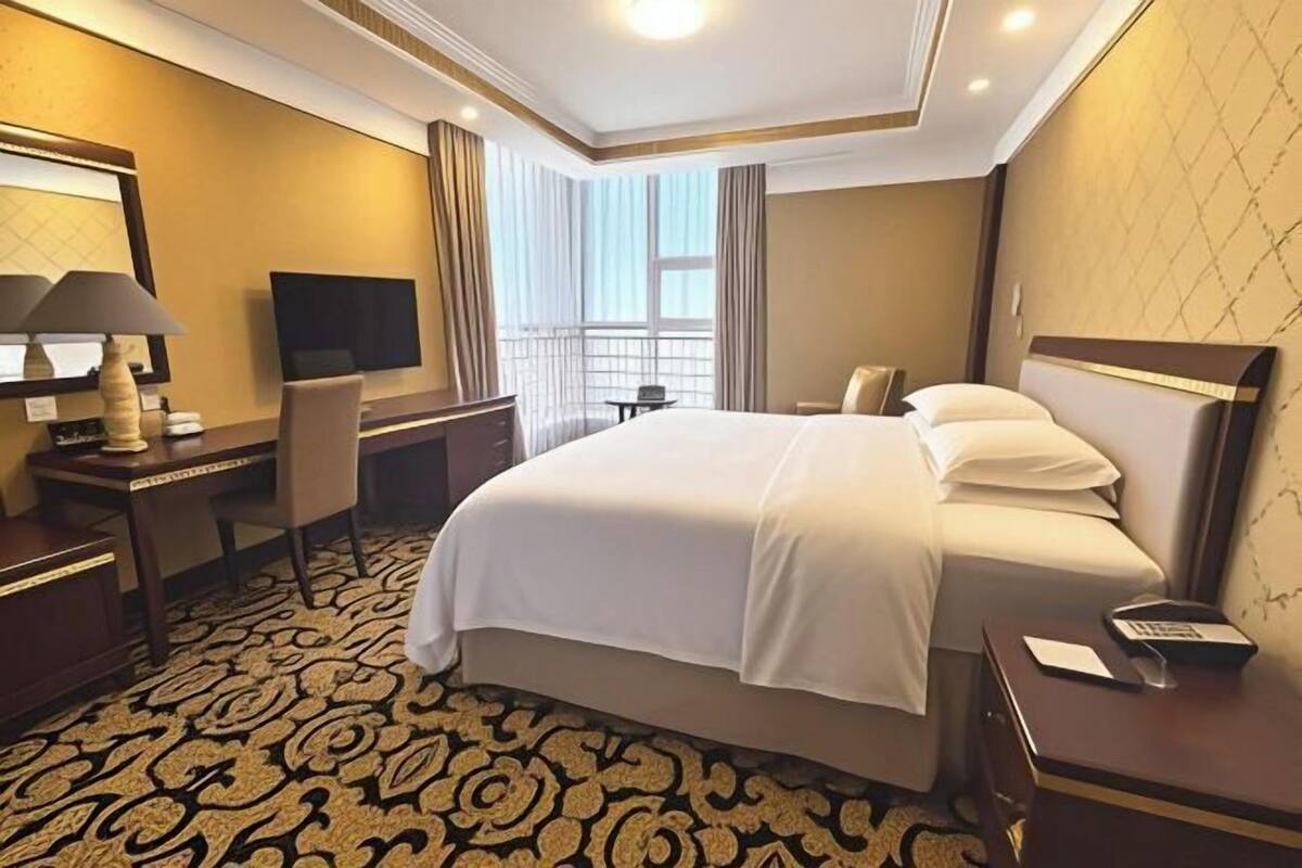 A hotel room with a large bed, a desk with a lamp, a TV, and a window with curtains.