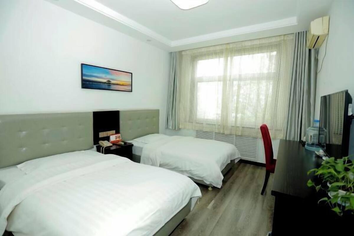 A hotel room with two beds, a desk, a chair, a TV, and a window with curtains.