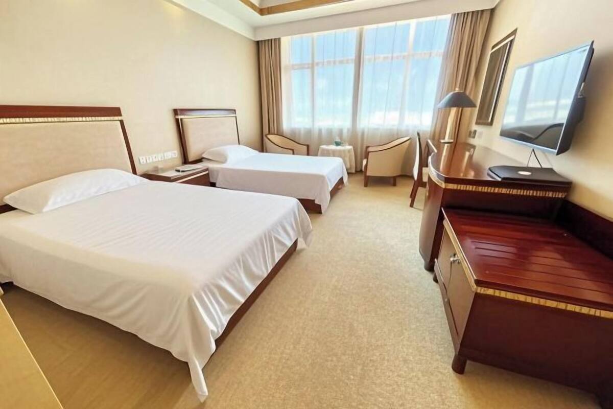 A hotel room with two beds, a desk, a chair, a TV, and a small table.