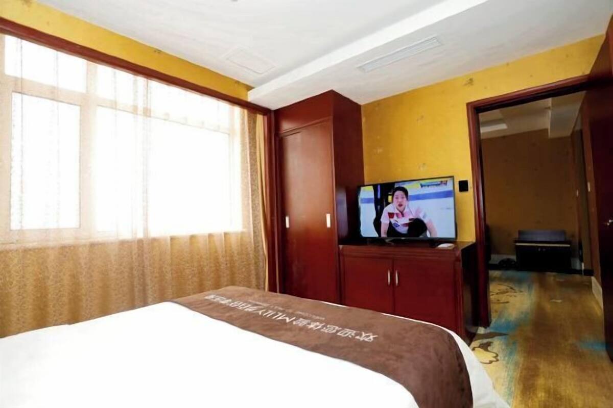 A hotel room with a bed, a television, a wardrobe, and a door leading to another room.