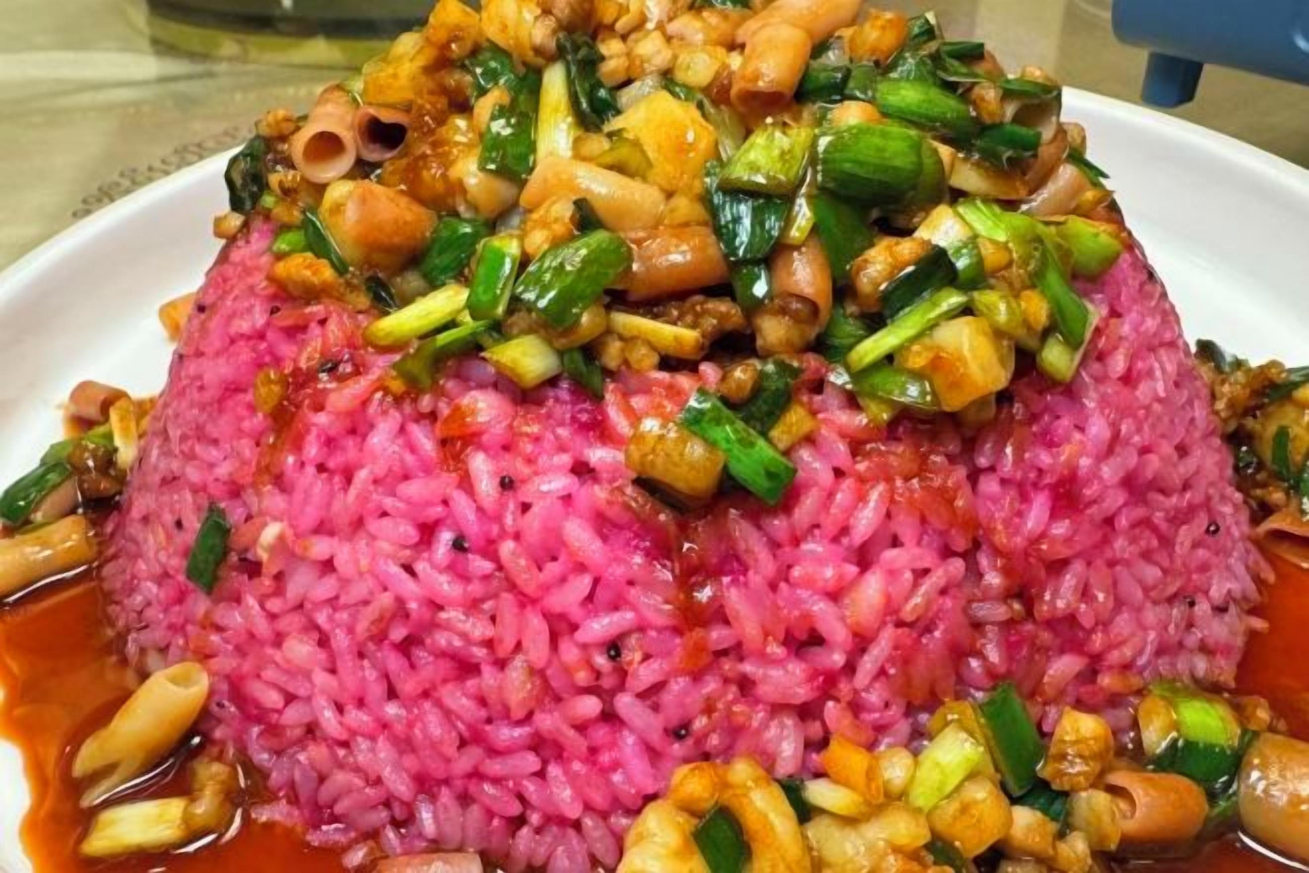 A plate of pink rice with vegetables and nuts.