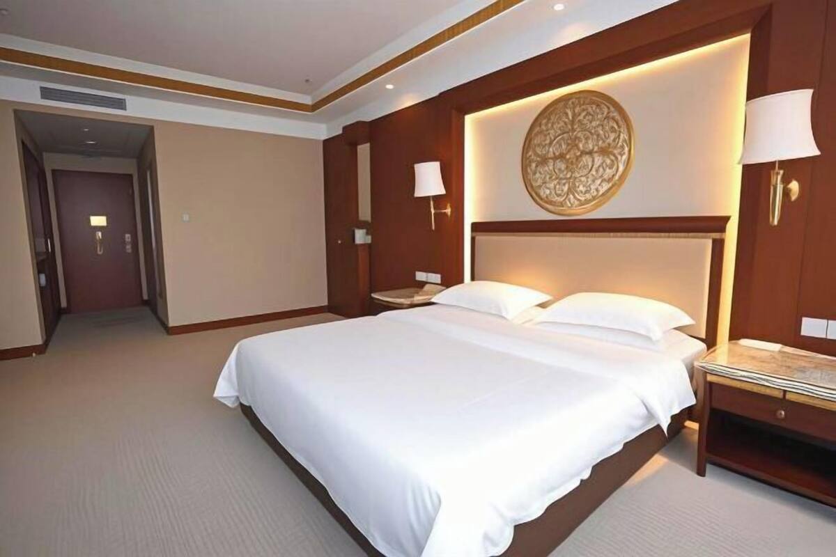 A hotel room with a large bed, a nightstand, a wall-mounted lamp, and a decorative wall piece.