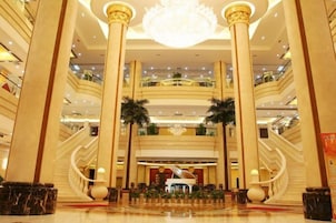 A multi-level hotel lobby with a grand staircase, palm trees, and a chandelier.