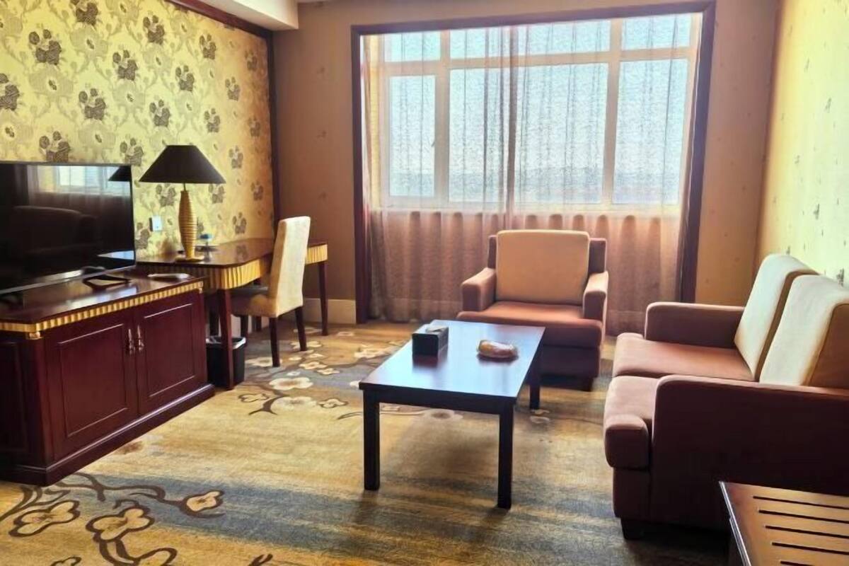 A living room with a television, a coffee table, a sofa, and a window with curtains.