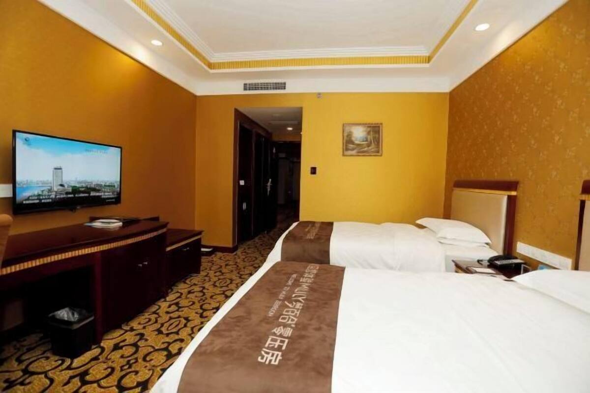 A hotel room with a bed, a desk, a television, and a painting on the wall.