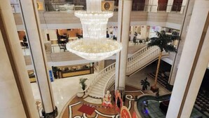 A multi-level atrium with a grand chandelier, a central staircase, and a pool area. - Gulf Hotel (Longkou)