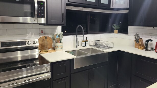 A modern kitchen with stainless steel appliances, a double sink, and dark cabinetry. - Modern Sunset Oasis - 2BD Apt w/ Pool & Views, 5 Min to Dining & Shopping (Kingston)