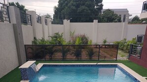 A rectangular swimming pool with blue mosaic tiles, surrounded by artificial grass and a low wall with a metal gate. - Modern Sunset Oasis - 2BD Apt w/ Pool & Views, 5 Min to Dining & Shopping (Kingston)
