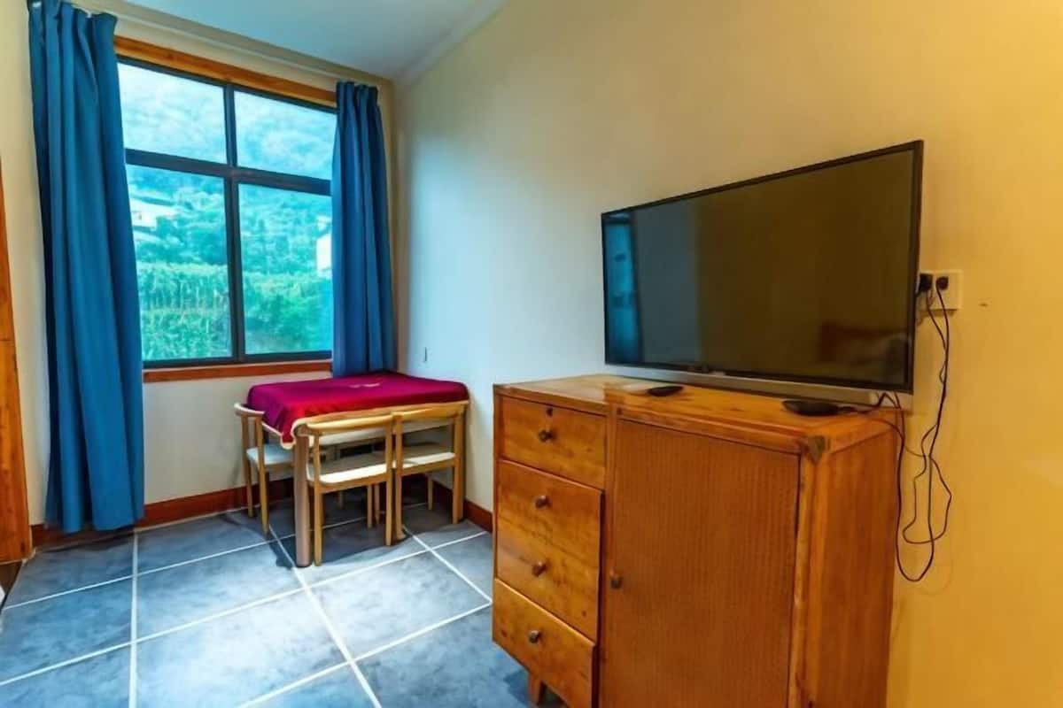 A room with a bed, a TV, a wooden cabinet, a window with curtains, and a tiled floor.