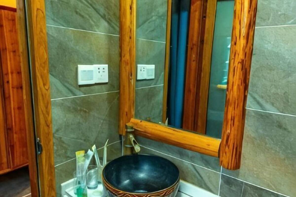 A bathroom with a wooden-framed mirror, a black basin, and tiled walls.