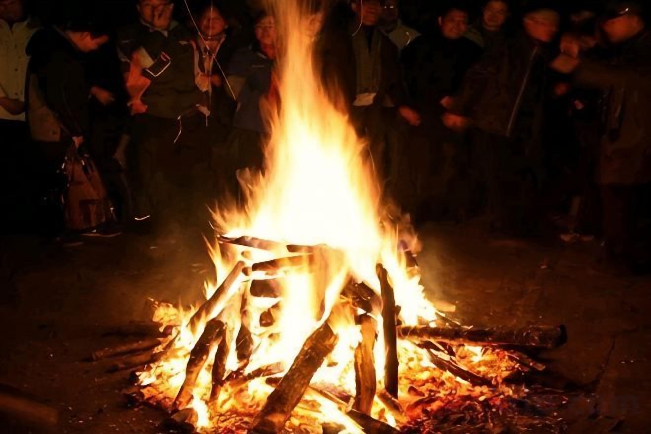 A campfire with logs arranged in a teepee shape, surrounded by people.