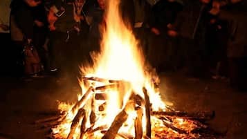 A campfire with logs arranged in a teepee shape, surrounded by people.