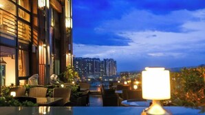 An outdoor seating area with tables and chairs, a lamp, and a view of high-rise buildings in the background. - Lotus Hotel (Sihui)