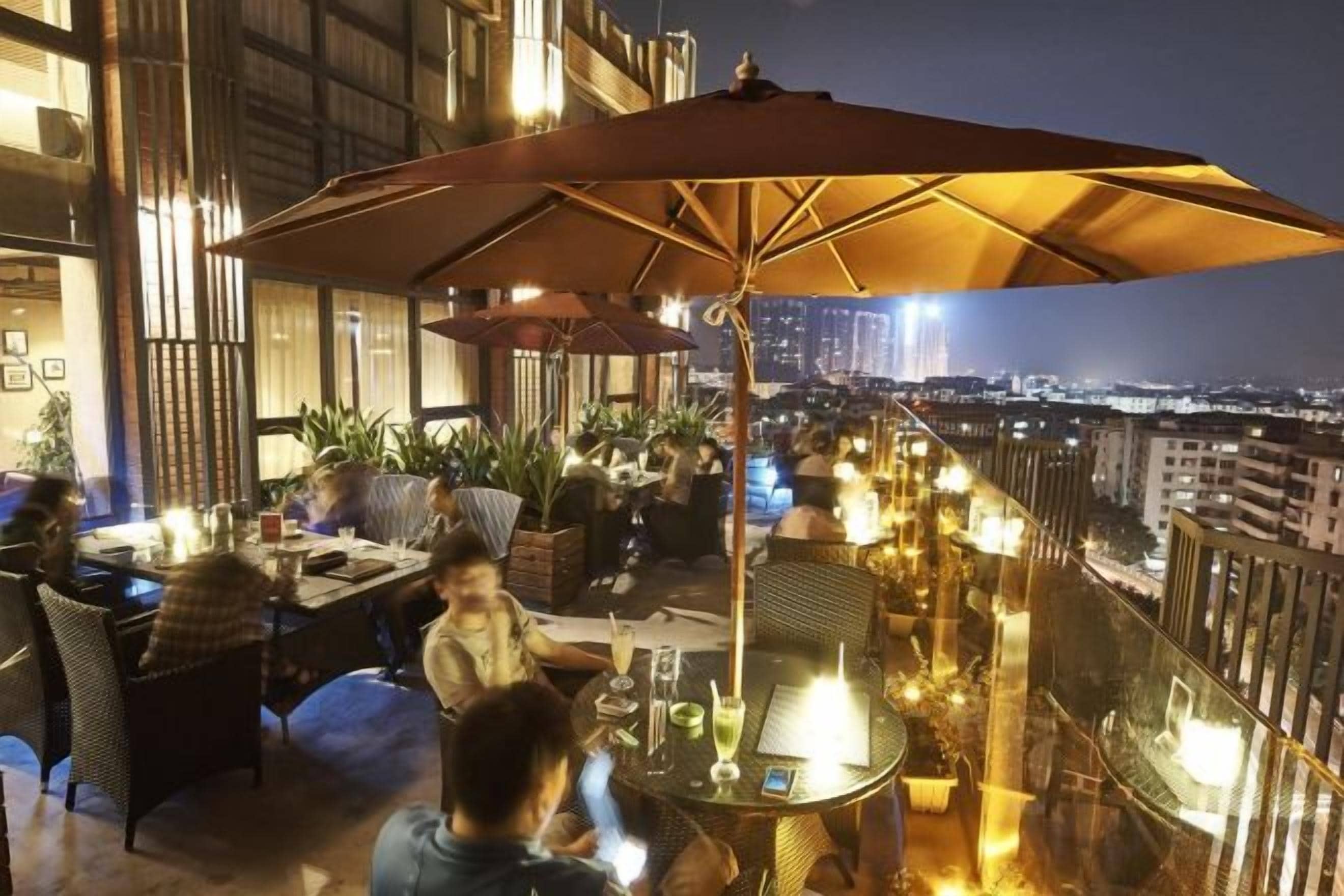 An outdoor dining area with tables and chairs, a large umbrella, and a city view.