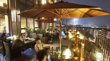 An outdoor dining area with tables and chairs, a large umbrella, and a city view.