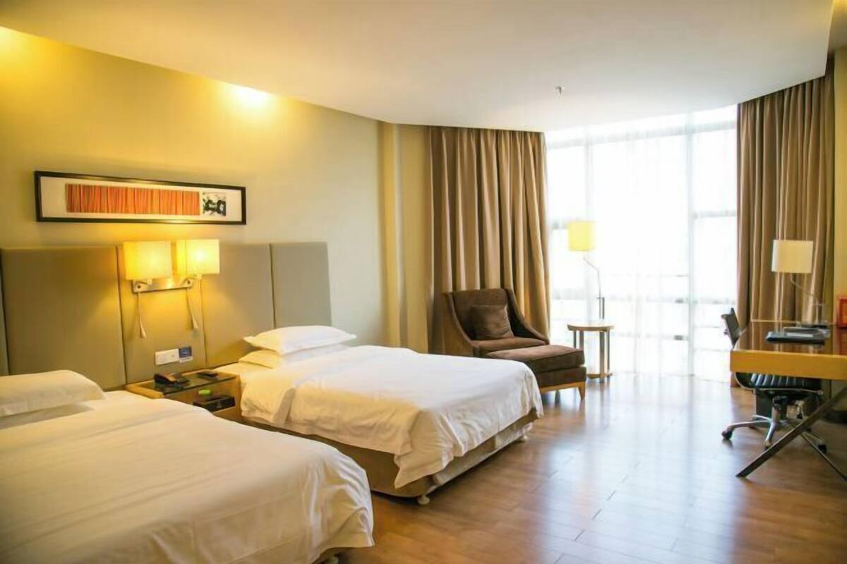 A hotel room with two beds, a desk, a chair, and a large window with curtains.