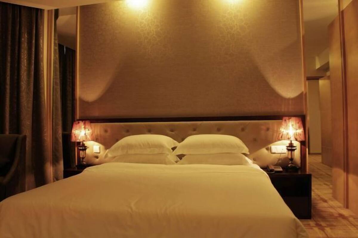 A hotel room with a large bed, two bedside lamps, and a headboard with a textured pattern.