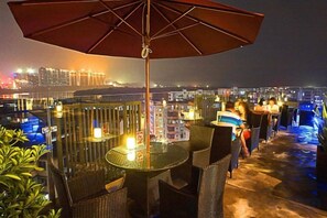 Una terrazza all'aperto con tavoli e sedie, un ombrellone grande e una vista sulla città sullo sfondo.