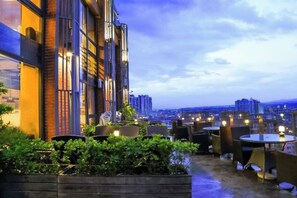 An outdoor seating area with tables and chairs, surrounded by greenery, and overlooking a cityscape. - Lotus Hotel (Sihui)
