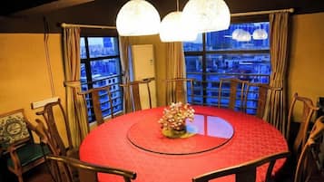 A round table with a red tablecloth, surrounded by wooden chairs, and a flower centerpiece.