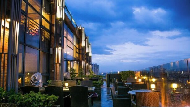 An outdoor seating area with wicker chairs and tables, overlooking a cityscape at dusk. - Lotus Hotel (Sihui)