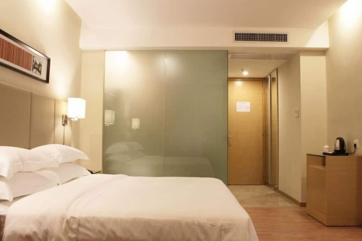 A hotel room with a bed, a nightstand, a mirror, and a door leading to a bathroom.
