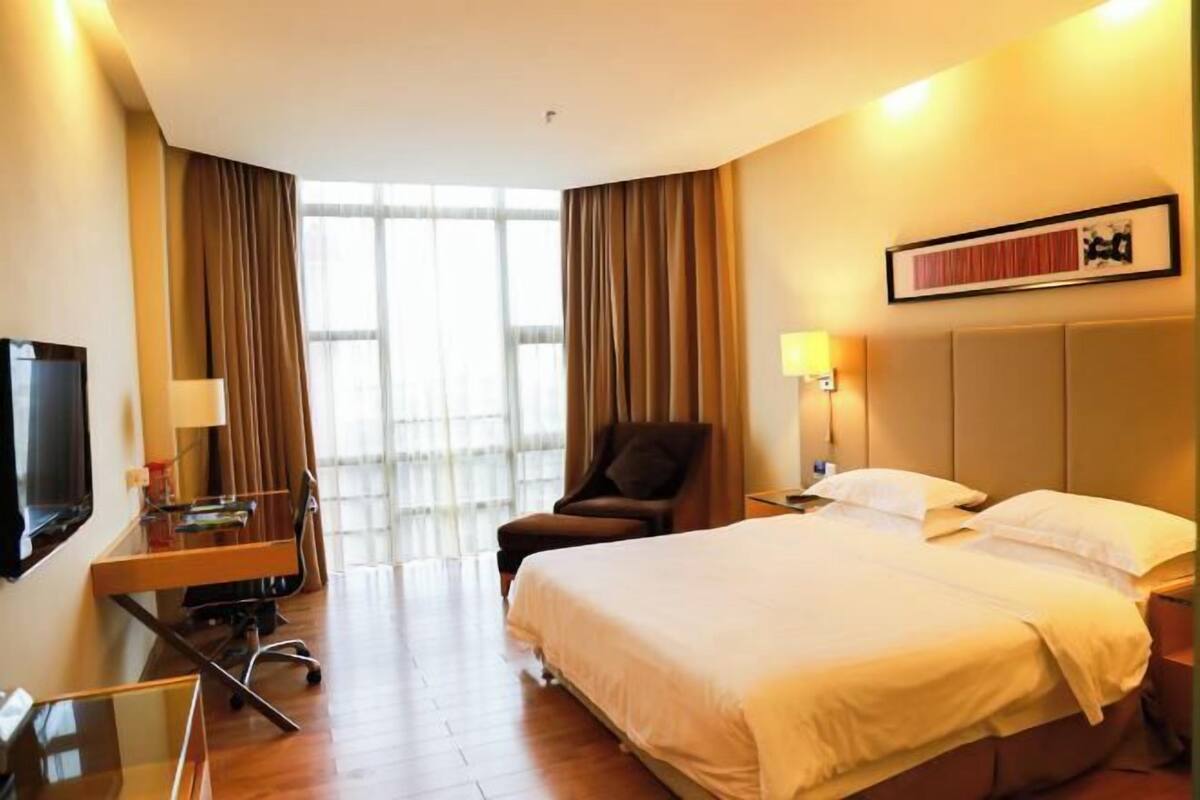 A hotel room with a large bed, a desk with a computer, a chair, a TV, and a window with curtains.