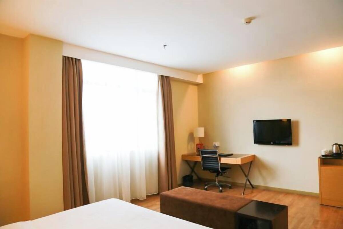 A hotel room with a bed, a desk, a chair, a television, and a window with curtains.