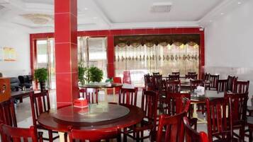 A hotel dining area with round tables and chairs, a large pillar, and a window with curtains.