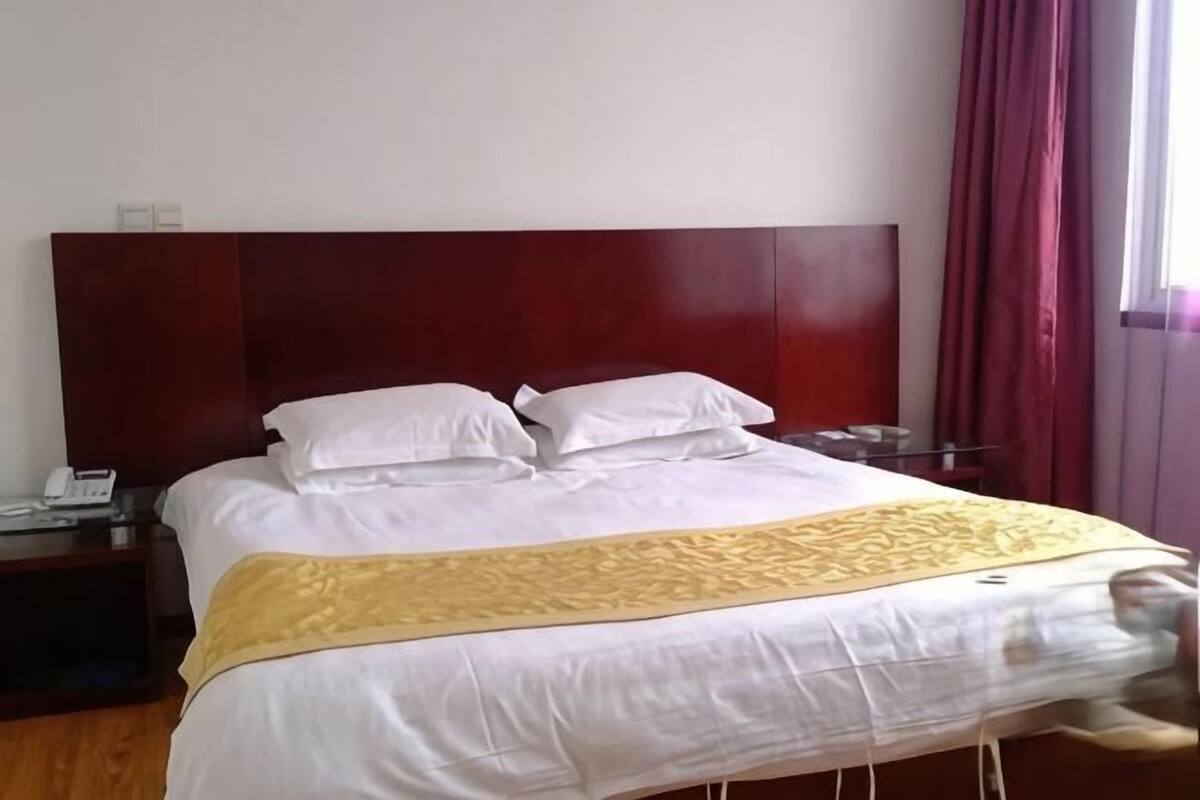 Hotellihuone, jossa on sänky, yöpöytä, puhelin ja ikkuna, jossa on verhot.