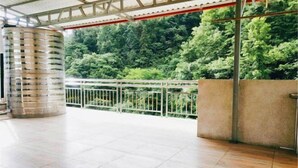 A covered outdoor area with tiled flooring, a metal railing, and a view of dense greenery. - Jianshi Hongshan Villa (Jianshi)
