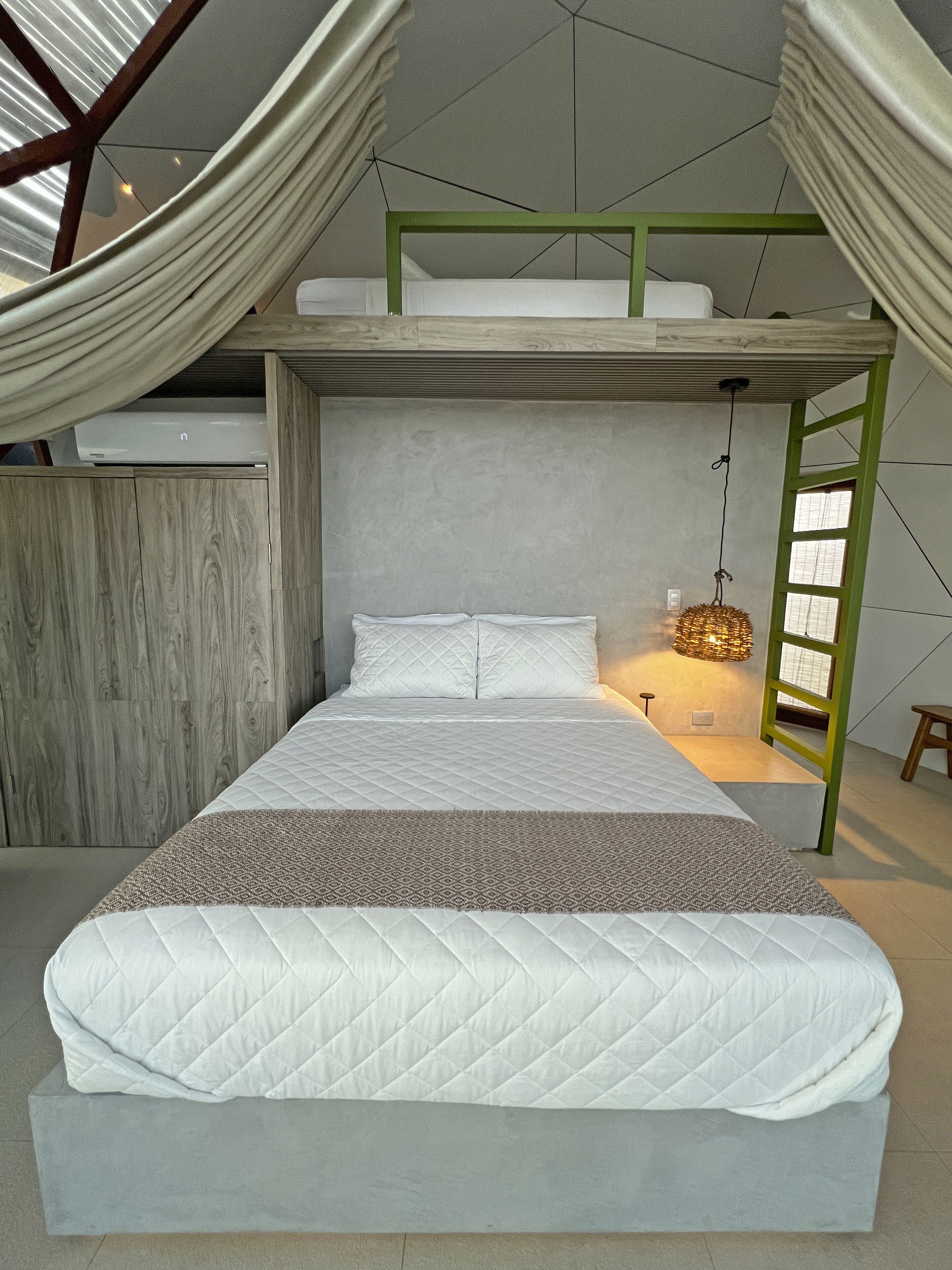 A modern loft bedroom with a bunk bed, a hanging light fixture, and a view of the sky through a large window.