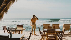 Um deck de madeira com mesas e cadeiras voltado para o oceano.
