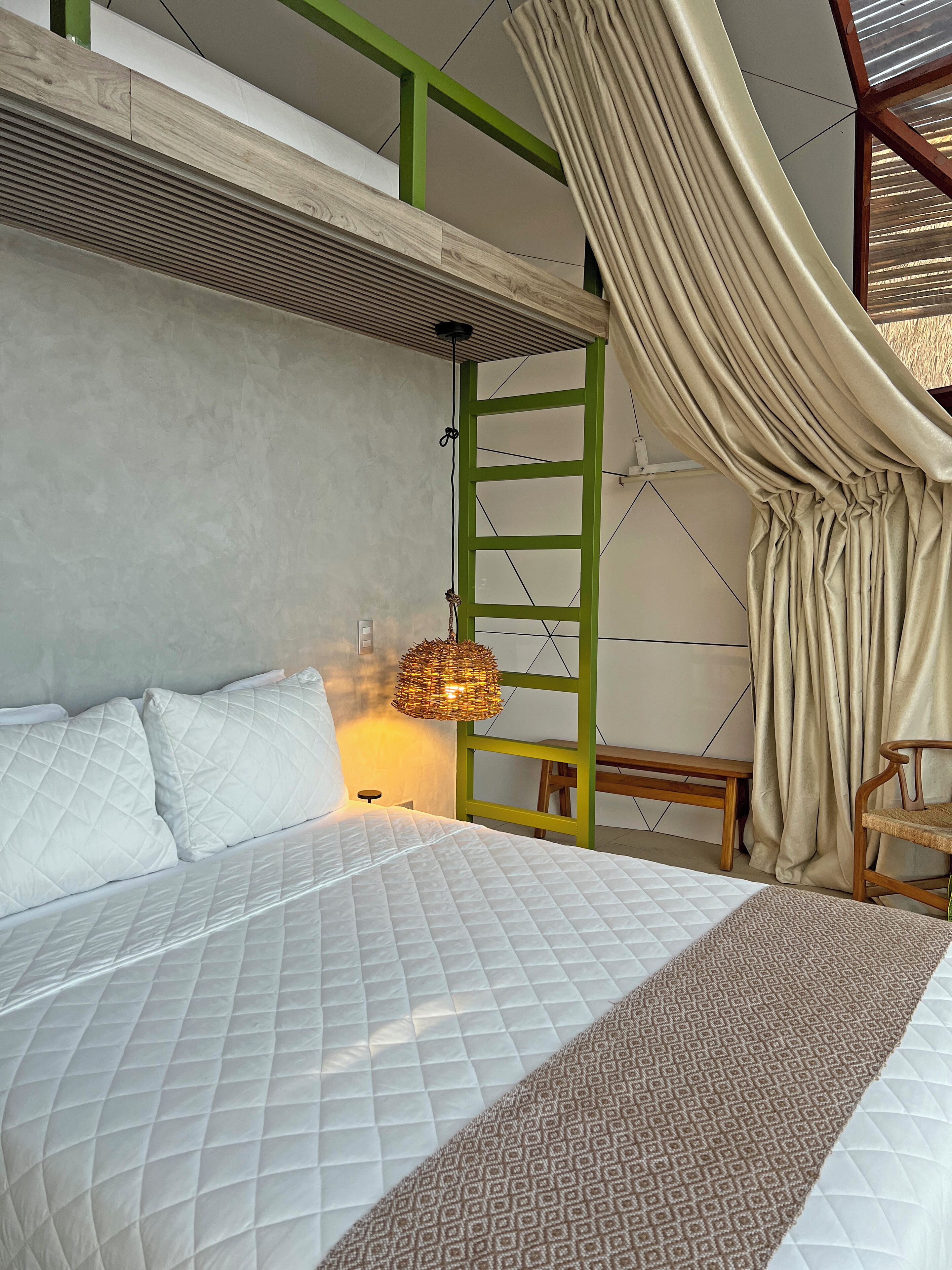 Un dormitorio con una cama, una lámpara colgante, un banco y una escalera.