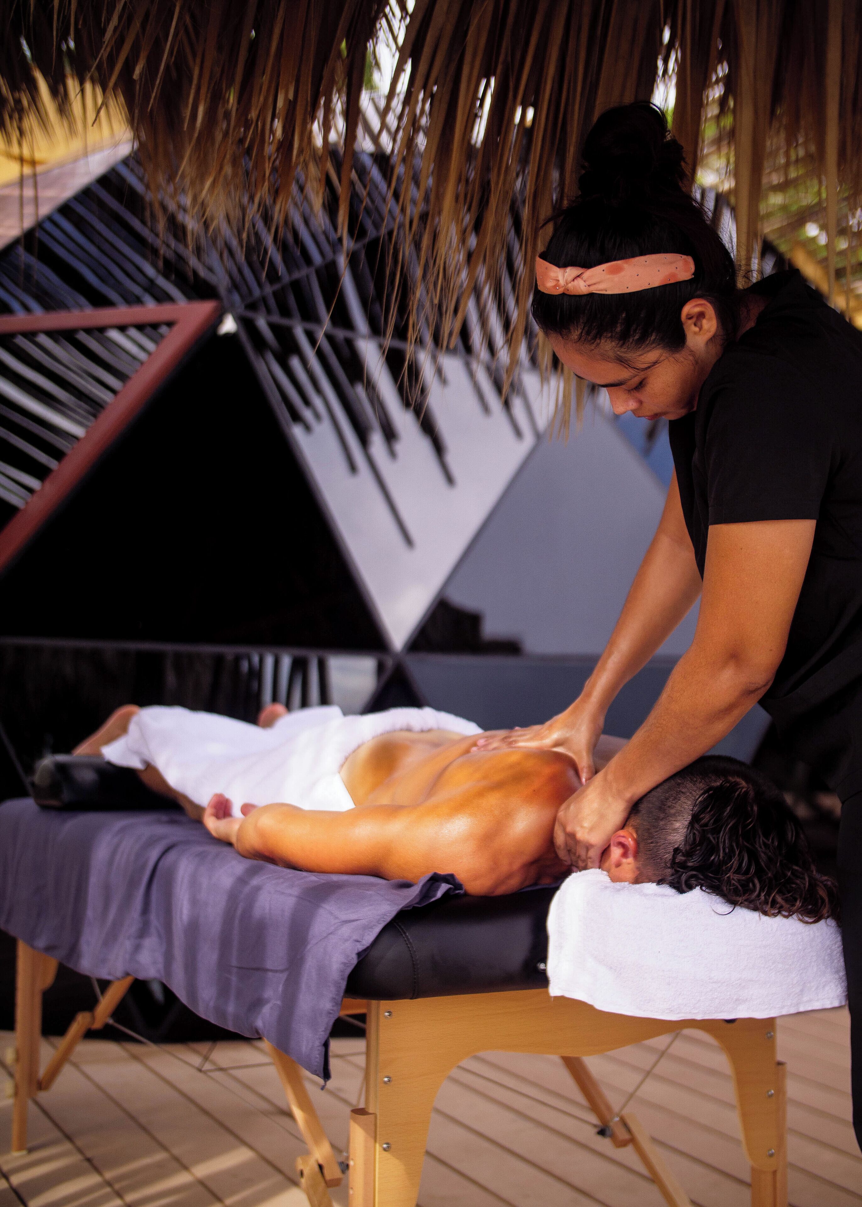 Een massagebehandeling in een ruimte met een houten vloer en rieten dak.