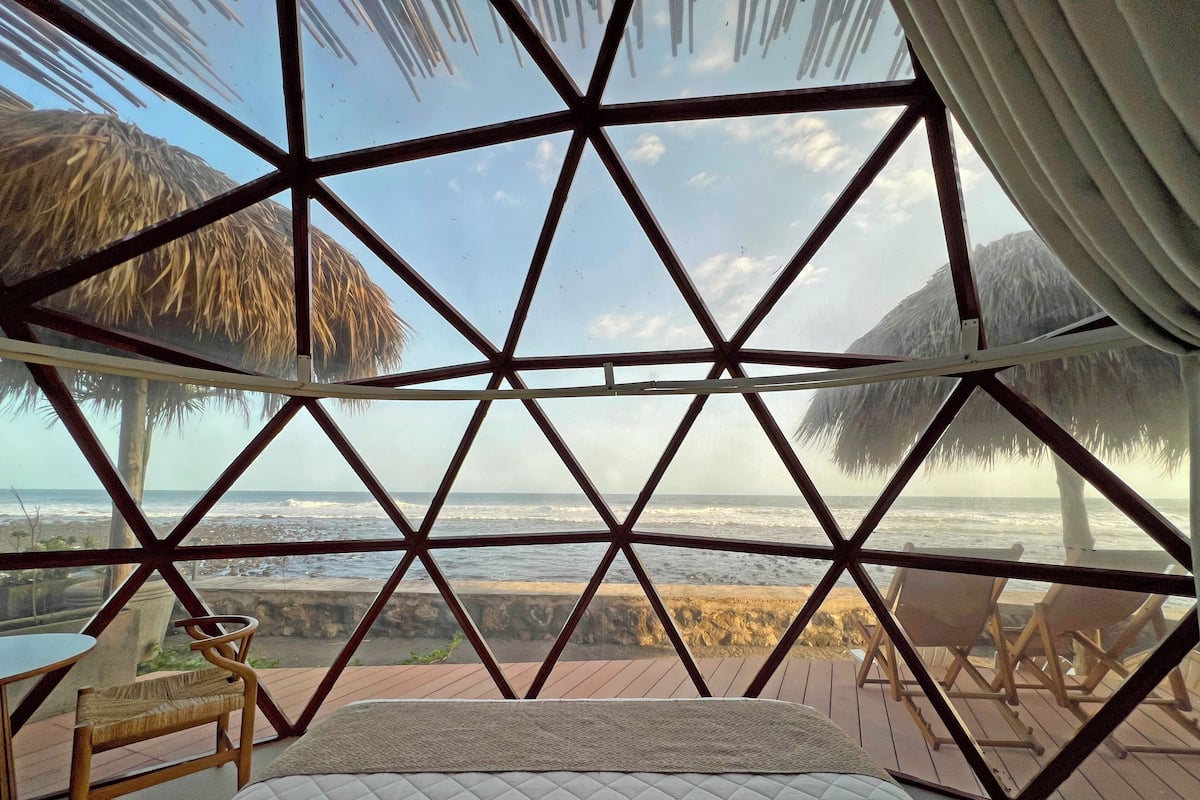 Quarto com janela de design geométrico com vista para uma praia.