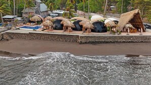 Um resort à beira-mar com palafitas de telhado de palha, piscina e palmeiras.
