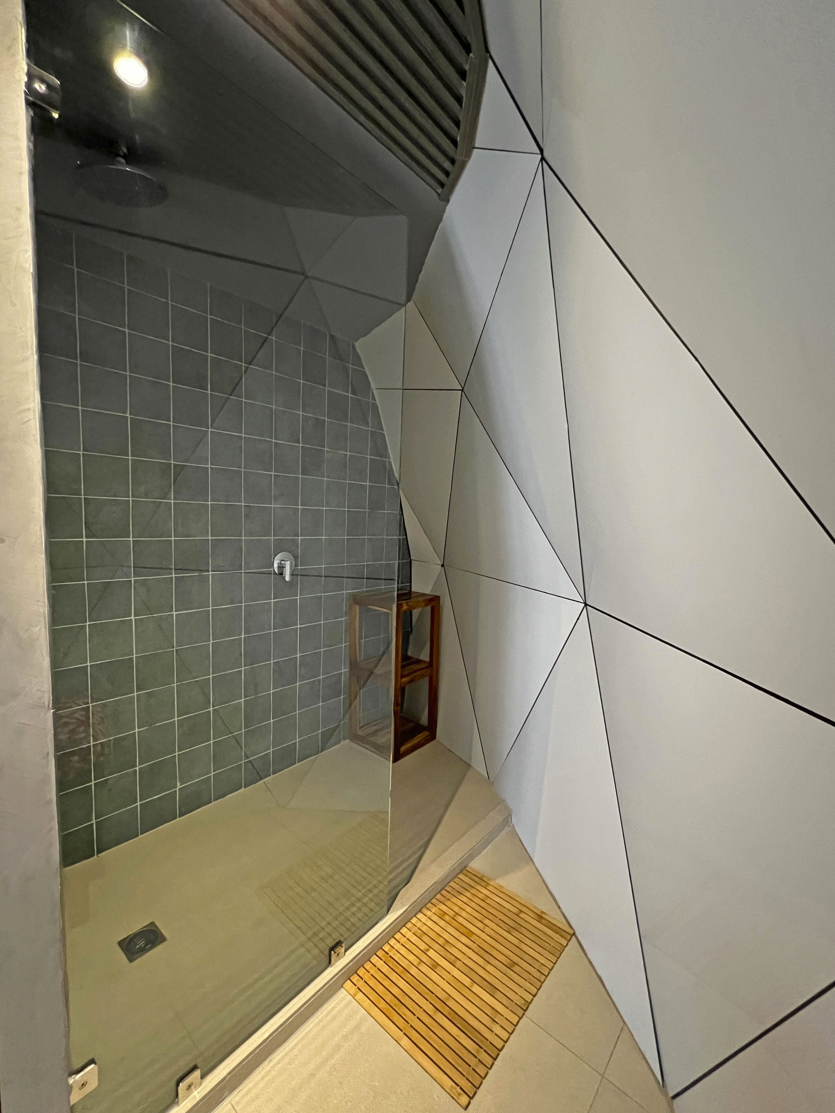 Un baño moderno con cabina de ducha de vidrio, paredes con azulejos y un banco de madera.