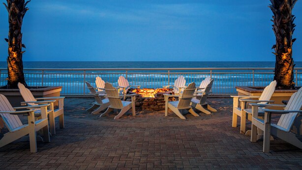 Un espace aménagé près de la plage, avec un foyer et des chaises disposées face à l’océan.