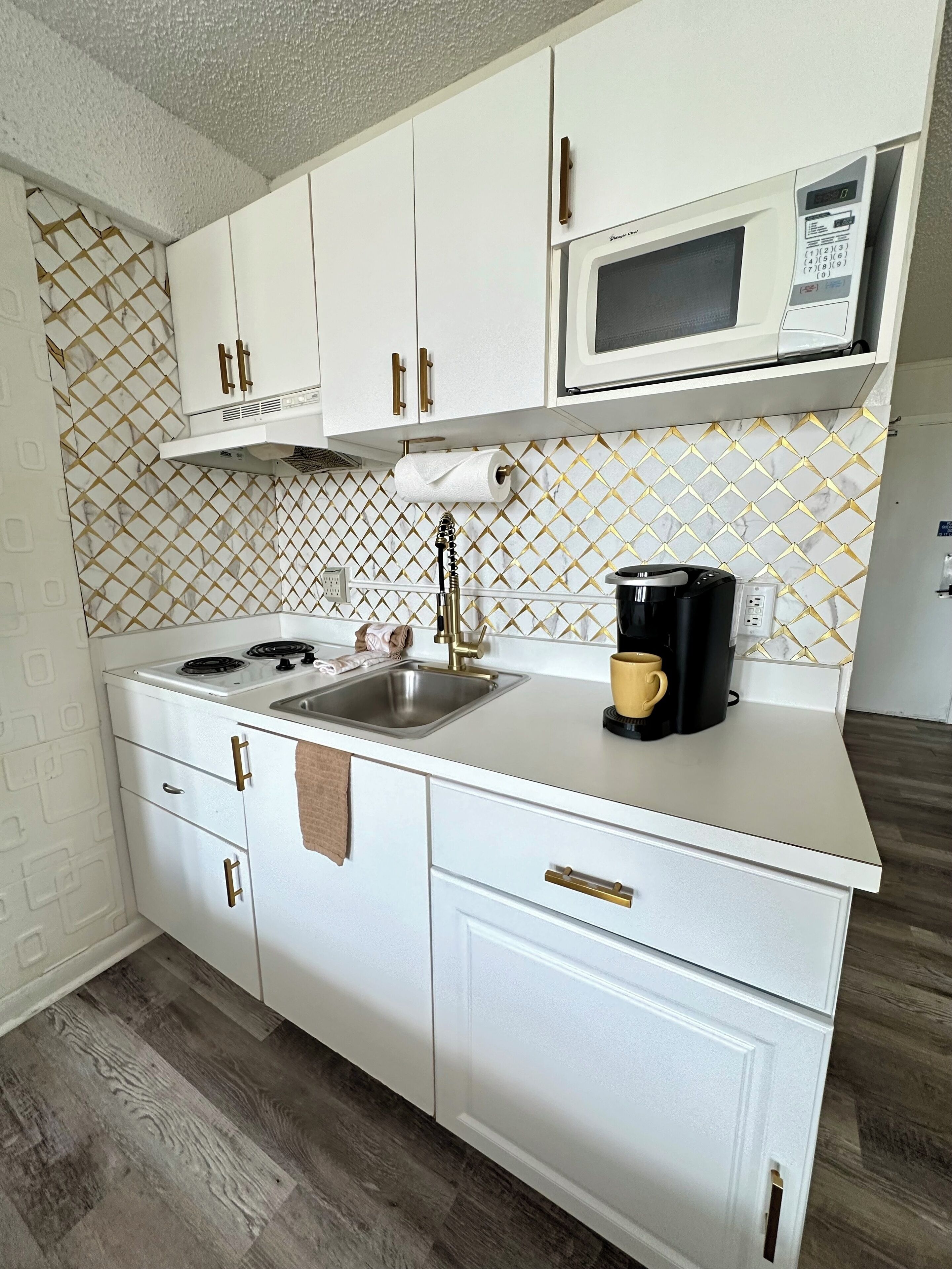 A compact kitchen with white cabinets, a stainless steel sink, a microwave, and a coffee maker on the countertop.